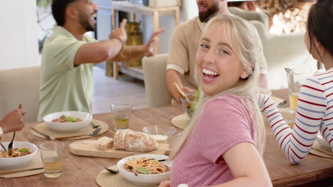 Eating pasta and laughing, young friends enjoying meal together at home