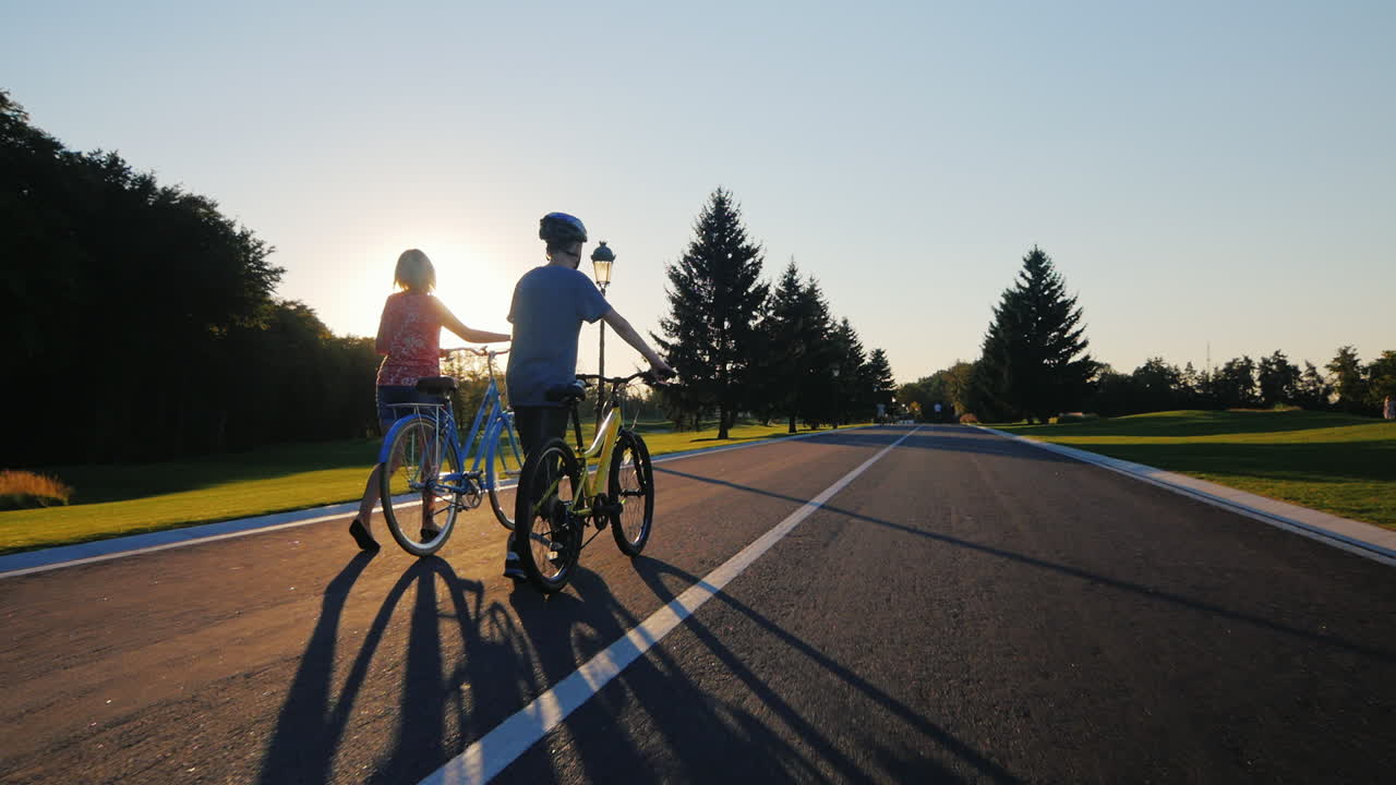 일몰에 자전거를 타고 공원을 산책하는 여자와 아들