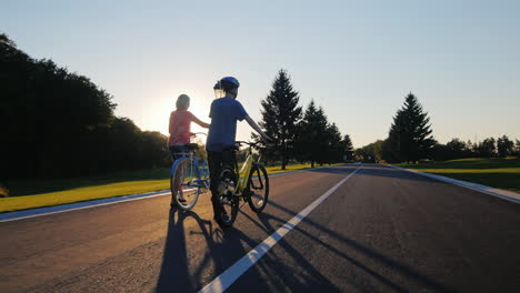 woman and son walking in the park with bikes on the sunset