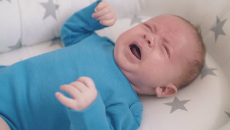 crying little baby lies in cocoon with grey stars at home