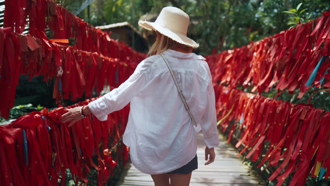 Mujer caminando a través de un túnel de deseos con cintas rojas en un jardín tropical