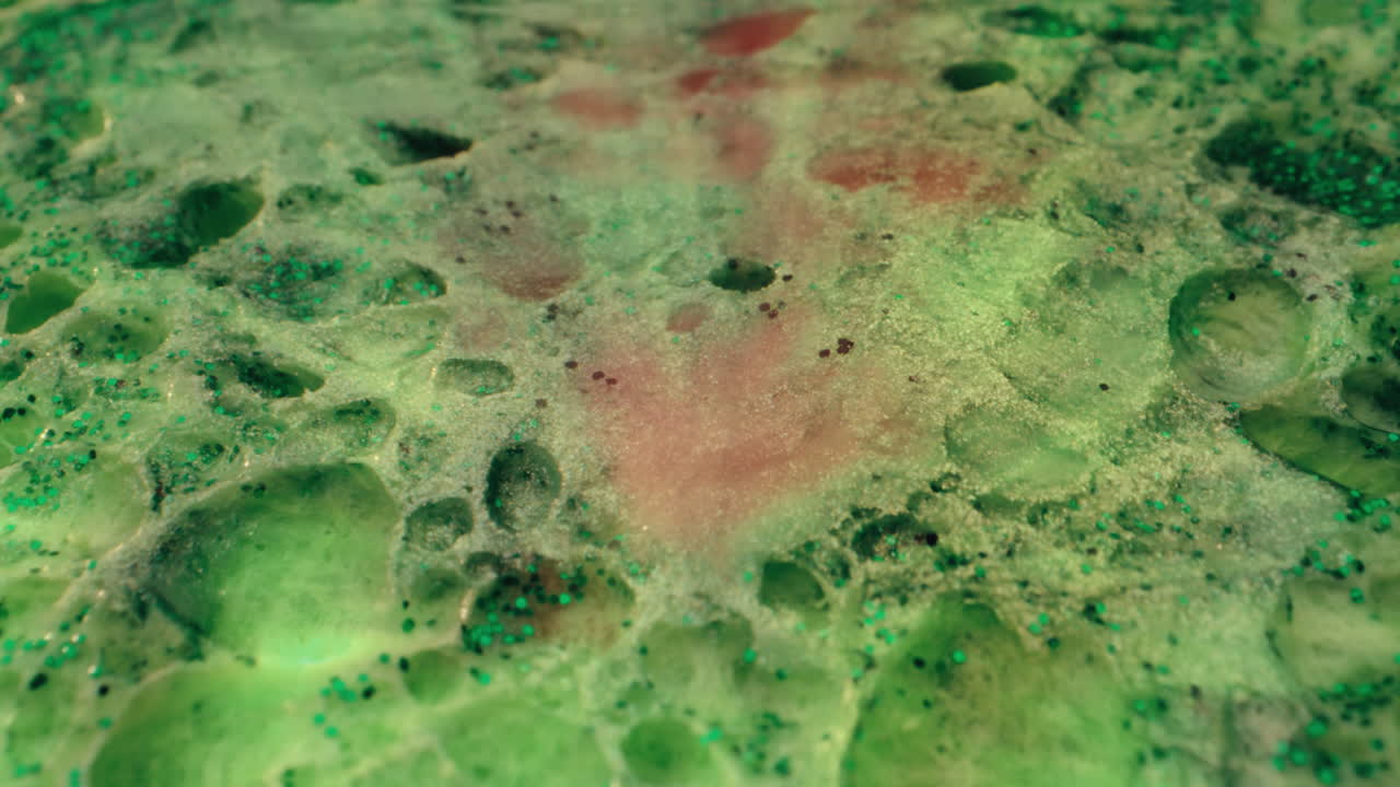 Close-up view of a textured, green, glittery surface with pink and red stains.