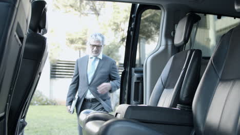 bearded businessman with laptop and notebook getting into car