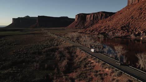 Luftaufnahme-Von-Indian-Creek,-Einem-Bekannten-Ziel-Für-Kletterer-In-Utah,-USA,-Während-Ein-Van-Anmutig-Die-Straße-Darunter-Entlangfährt-Und-Abenteuer-Und-Freiheit-Auf-Der-Offenen-Straße-Vereint