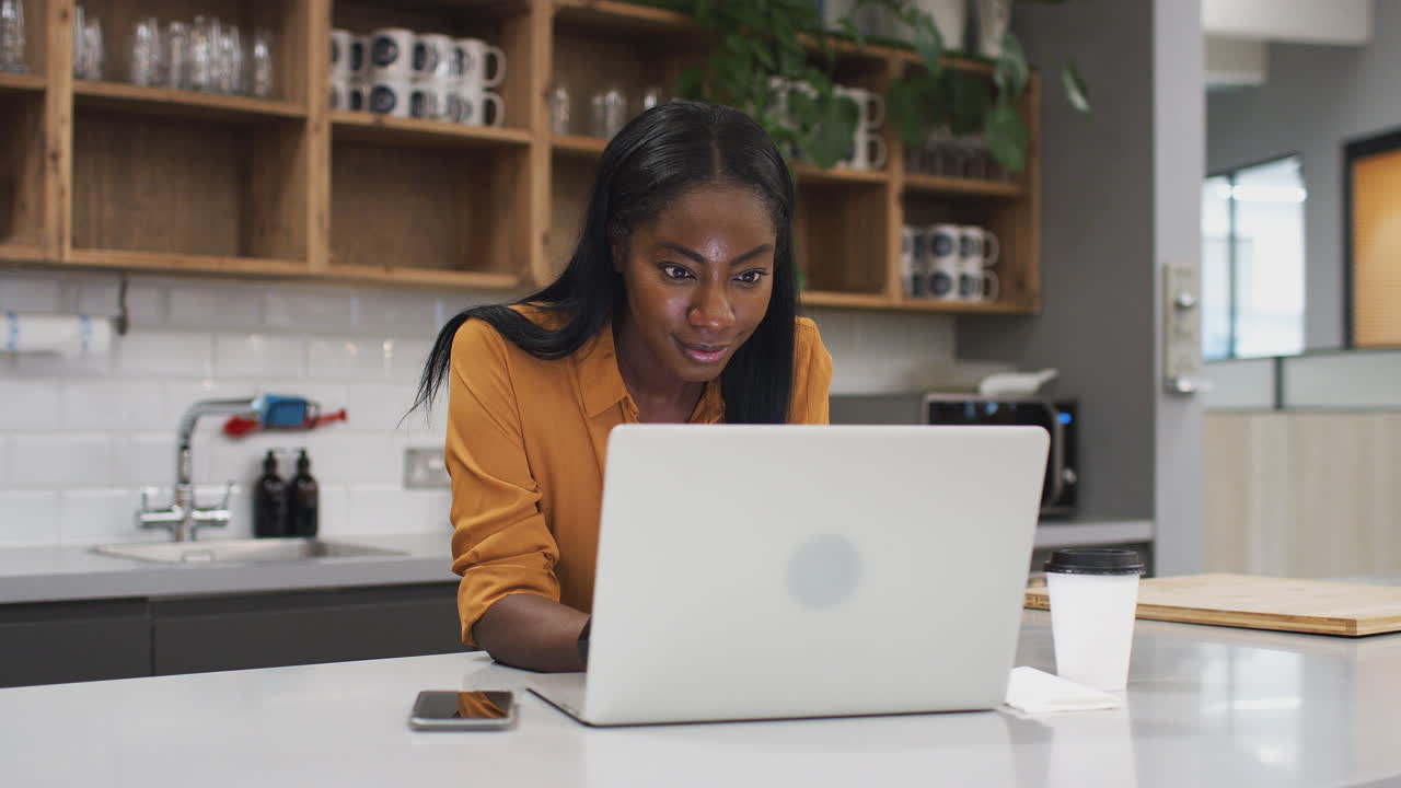 Businesswoman Working On Laptop In Kitchen Area Of Modern Office