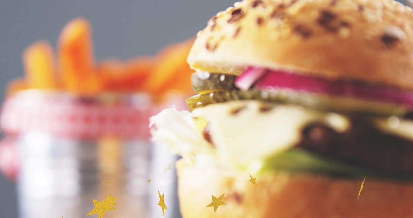 金色の星が漂い、カメラが右に移動する中、フライドポテトがぼやけ、ハンバーガーがスライドして焦点が合い、メニューが表示される。