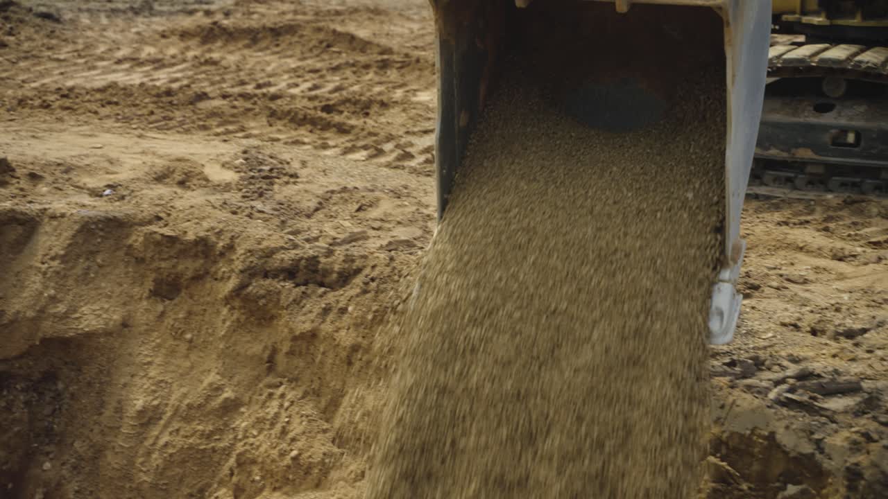 Gravel pours from excavator bucket into trench for pool base layer prep