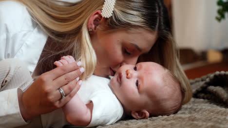 blonde long-haired woman with her newborn baby. mother leans to her child's face caressing little kid. close up.