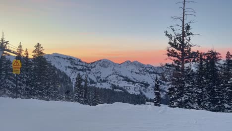 Handheld-shot-of-a-stunning-winter-landscape-scene-looking-down-at-a-cloudy-snow-covered-valley-during-a-golden-sunset-from-the-summit-of-a-ski-resort-in-the-Rocky-Mountains-of-Utah-on-a-windy-evening