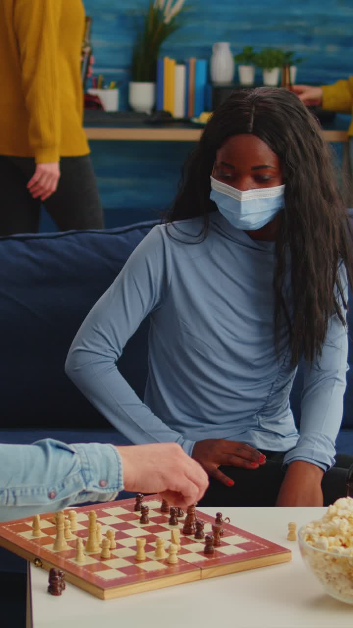 Vertical video: African woman wearing face mask playing chess with man