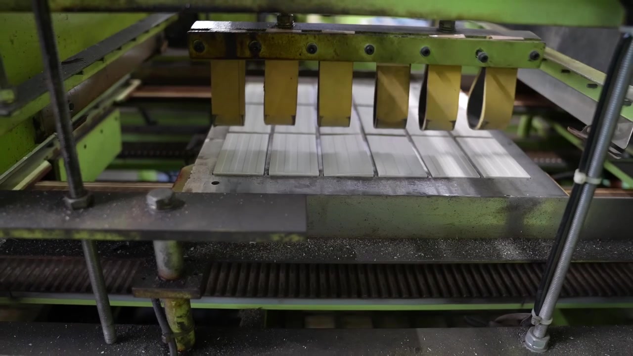 Yellow separator paddles lift between rows of white tiles on a ceramic factory conveyor