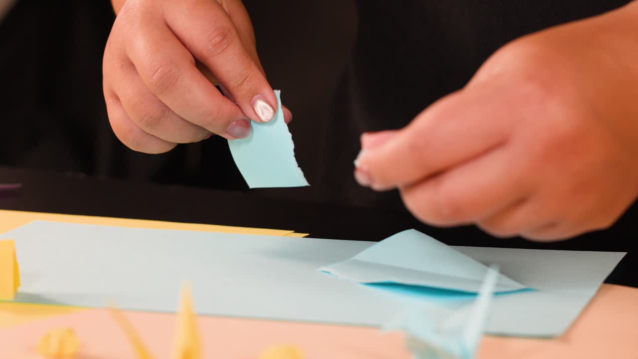 Primo piano di mani che piegano e strappano con cura carta blu per un progetto di origami