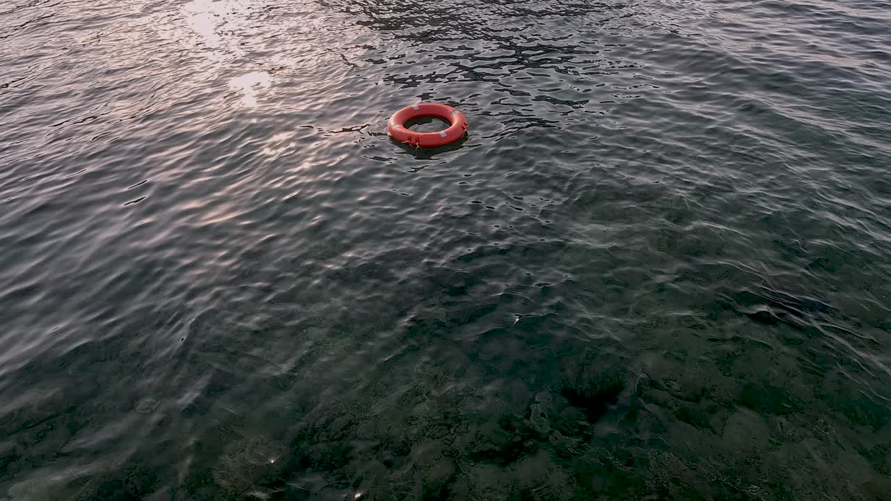A bright orange ring drifts quietly in serene waters as the sun sets, casting warm colors across the surface. Nature's tranquility is beautifully captured in this moment