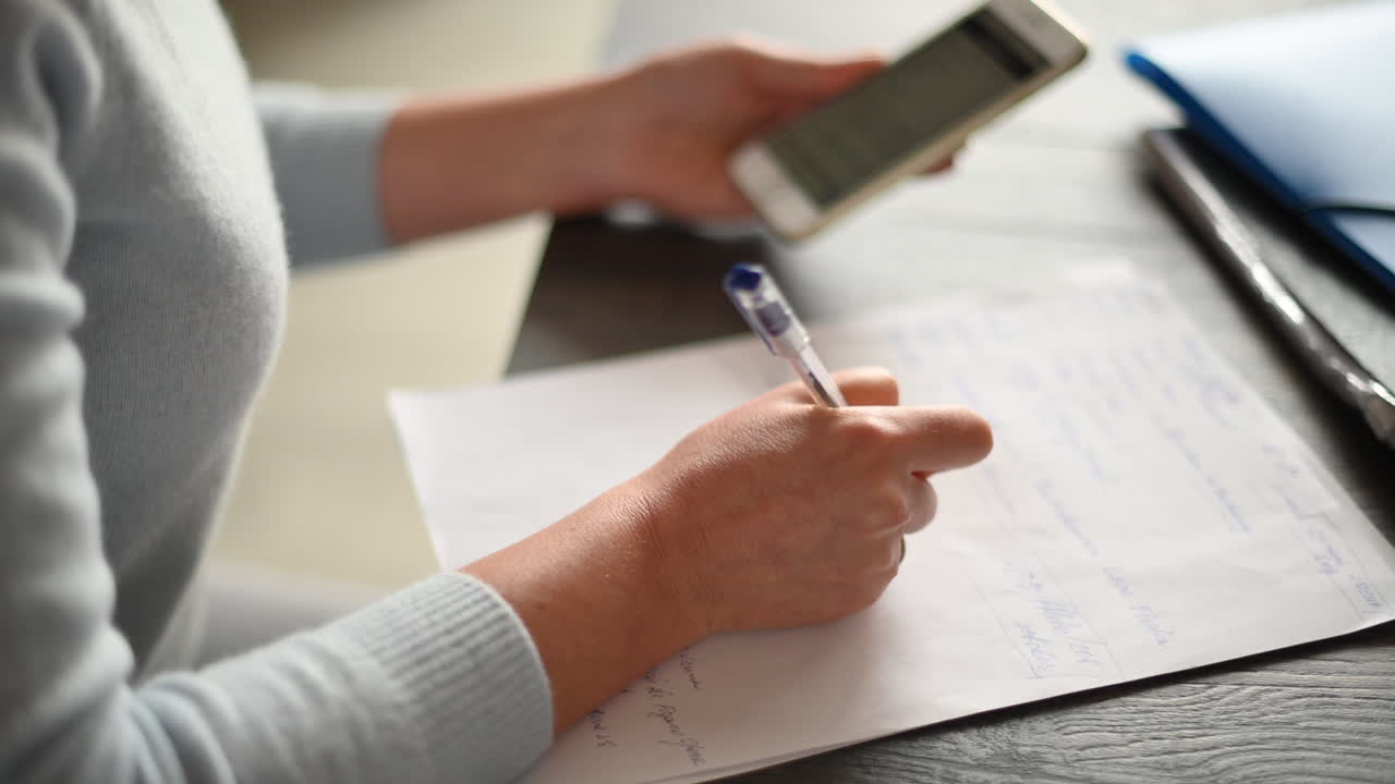Woman working on mobile phone and writing at the office