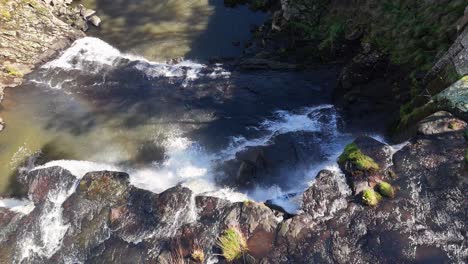 drone footage captures water flowing over rocky ledges at ebor falls, new south wales, with sunlight reflecting on the surface and lush greenery nearby