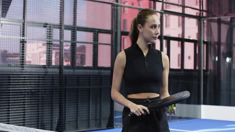 focused woman holding padel racket and ball on indoor court, ready to play, copy space