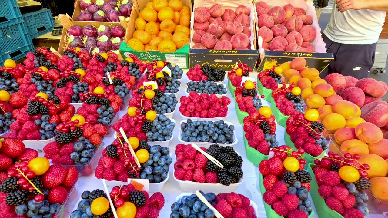 Assortimento colorato di frutti di bosco freschi e pesche esposti su una bancarella del mercato a Praga, filmato con un fluido movimento della telecamera verso il basso sotto la luce naturale del giorno.