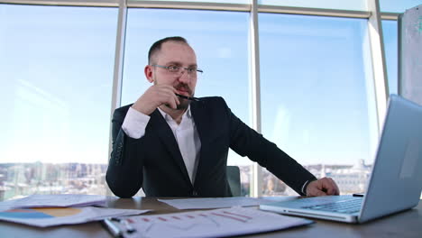 smiling boss sitting at table. bearded businessman in suit talking positively to someone in office room and smiles. business concept.