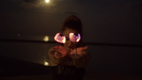 woman twirling fire palm torches against full moon lit lake, night exterior medium shot slowmo