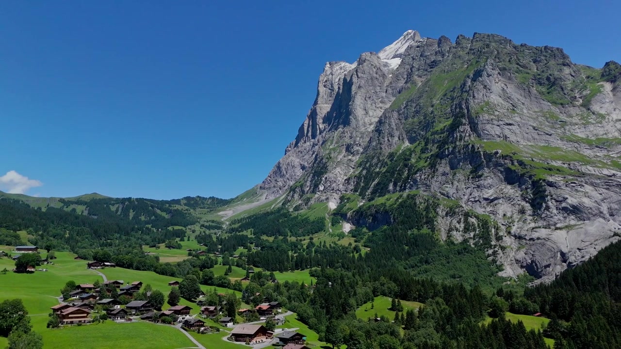 Rekaman drone sinematik terbang mundur untuk menampilkan puncak gunung yang menakjubkan dan lembah hijau Grindelwald. Pemandangan pegunungan Alpen yang indah di Swiss pada hari musim panas yang cerah