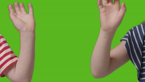 close up of two young children waving to camera against green screen 1