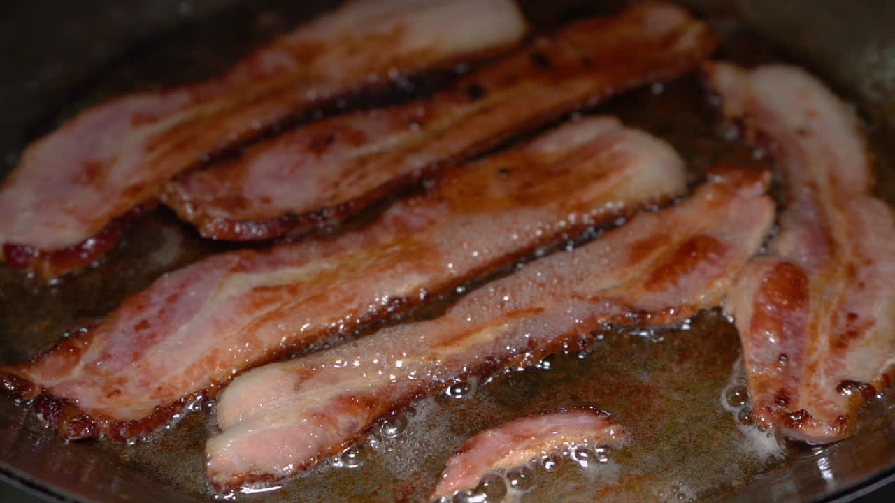 Slow motion clip of delicious bacon being fried in a stainless steel pan