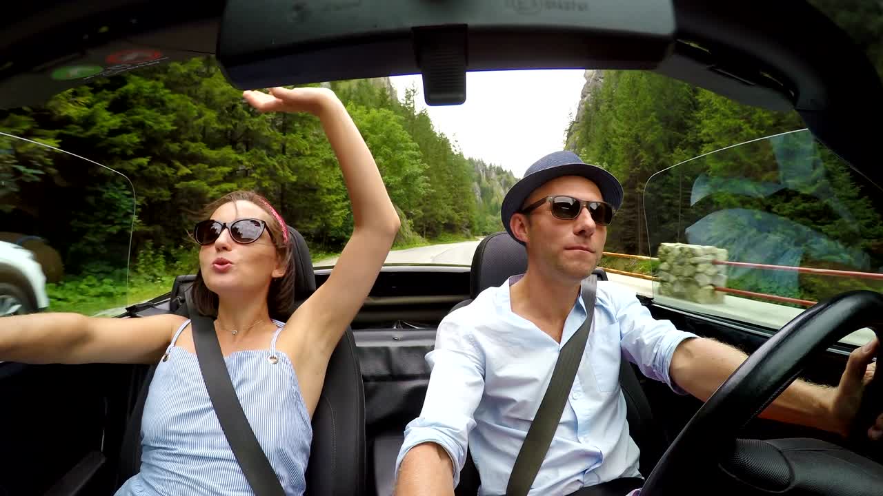video en 4k: una pareja feliz canta las canciones mientras el coche descapotable sin techo conduce por el camino de la montaña.