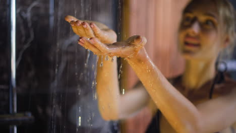 Young-woman-takes-shower-focus-on-hands-under-water-jets