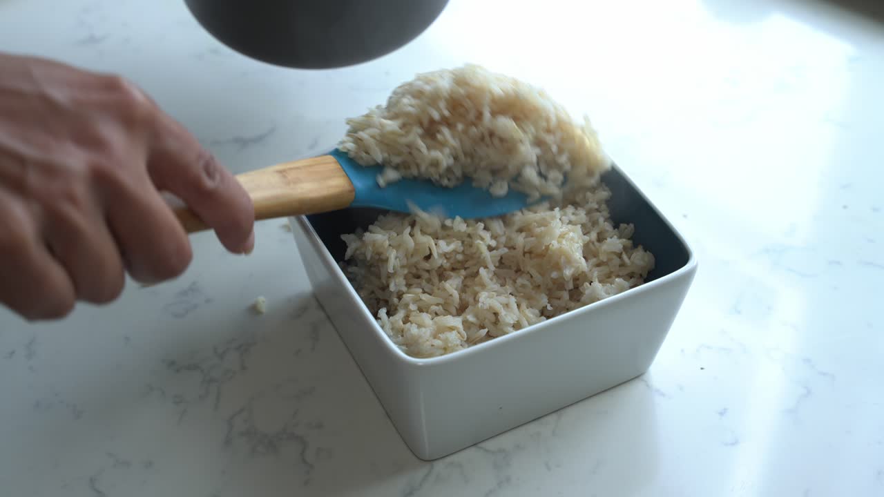 Close up shot of brown rice being plated inside of a bowl to cook a meal two cans of beans rice plantain avocado red onion and cilantro