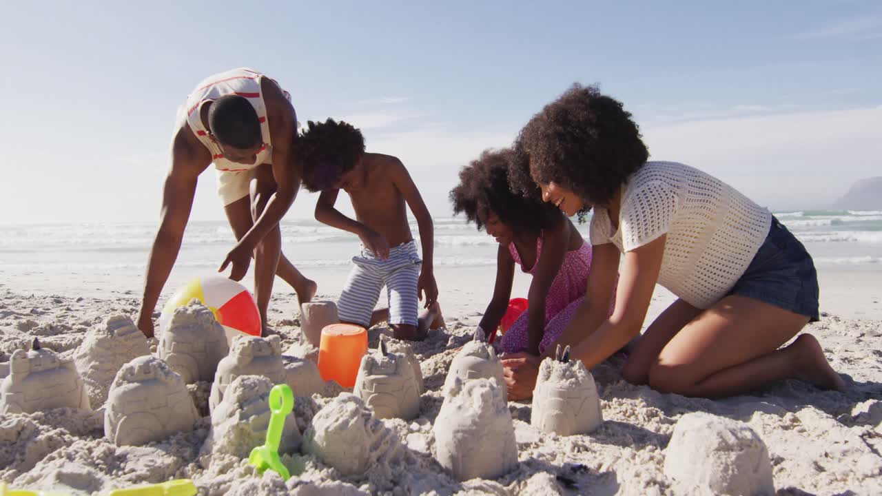 Pais afro-americanos e seus filhos brincando com areia na praia.