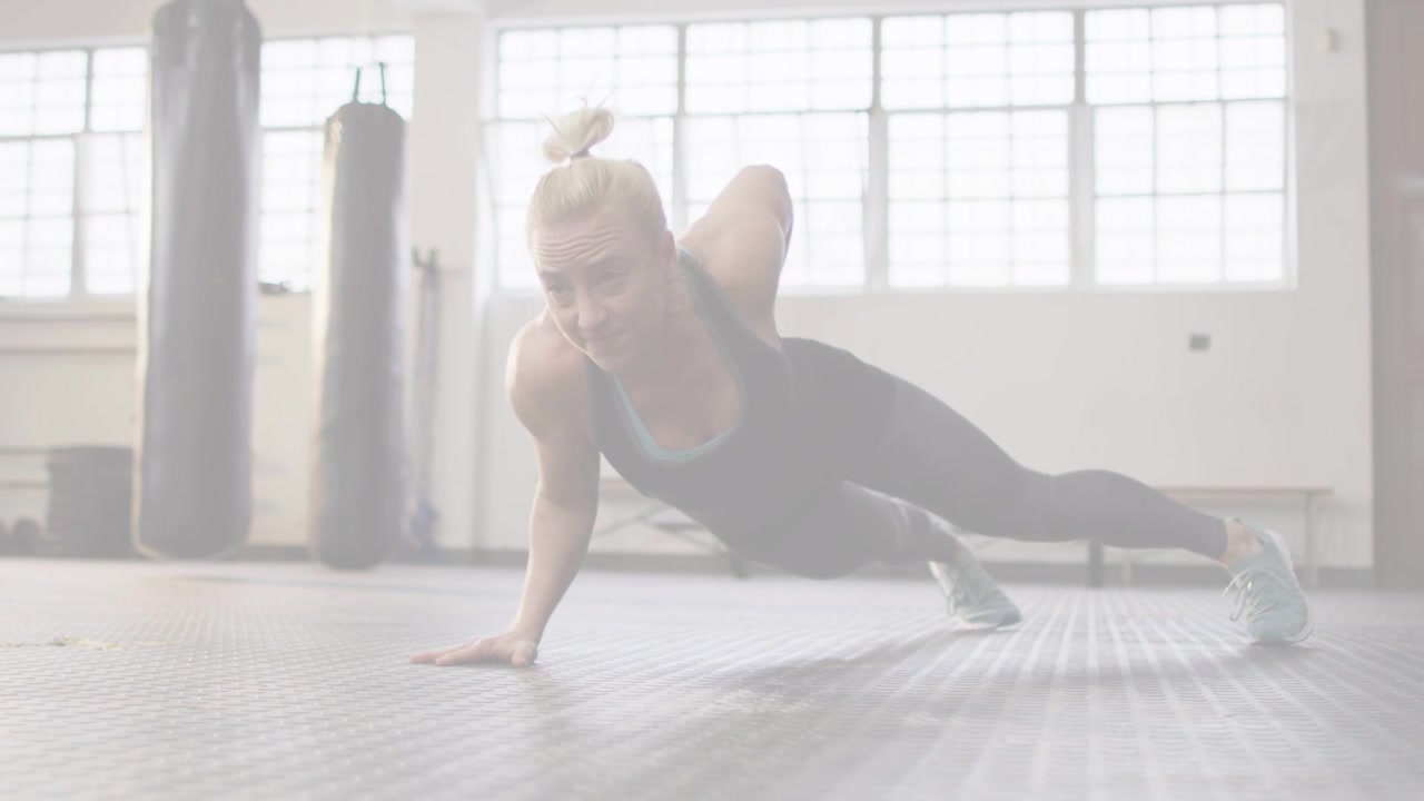 Donna che inizia da un plank alto e passa a un plank laterale su pavimento in gomma, attivando il core in palestra.