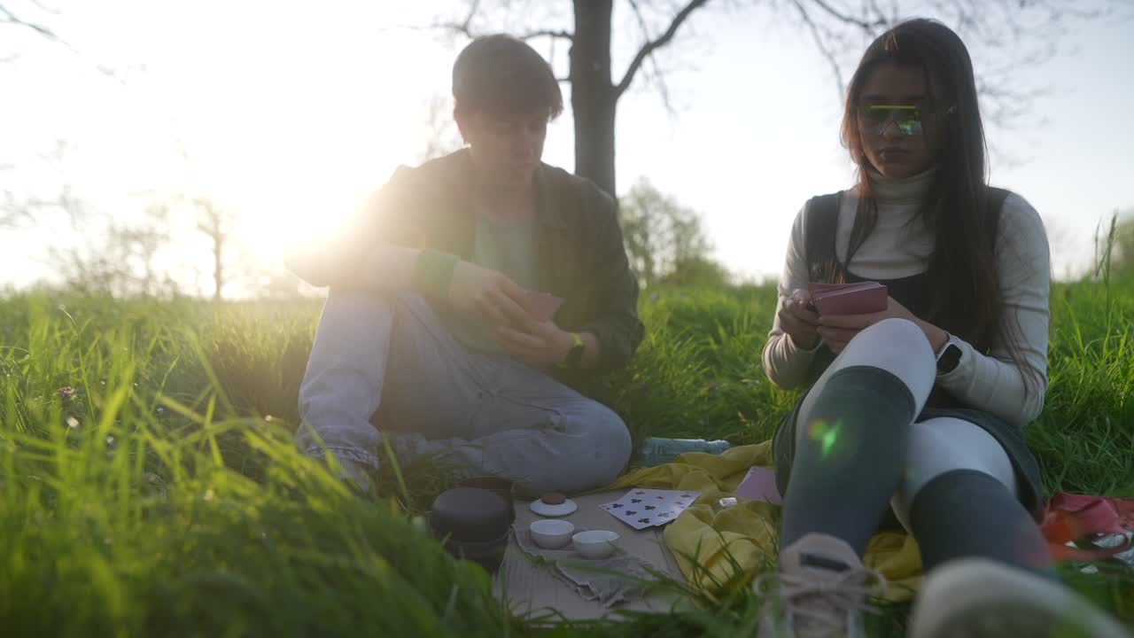 Friends Enjoying a Picnic and Playing Cards in a Park at Sunset