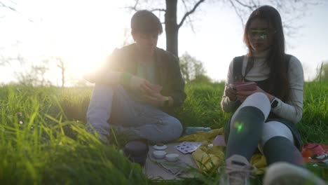 friends enjoying a picnic and playing cards in a park at sunset