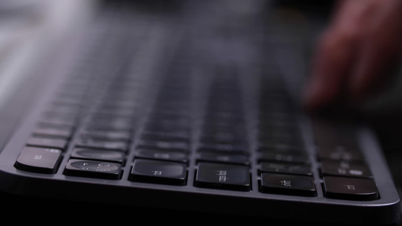 Hand typing on a black computer keyboard, close up side view