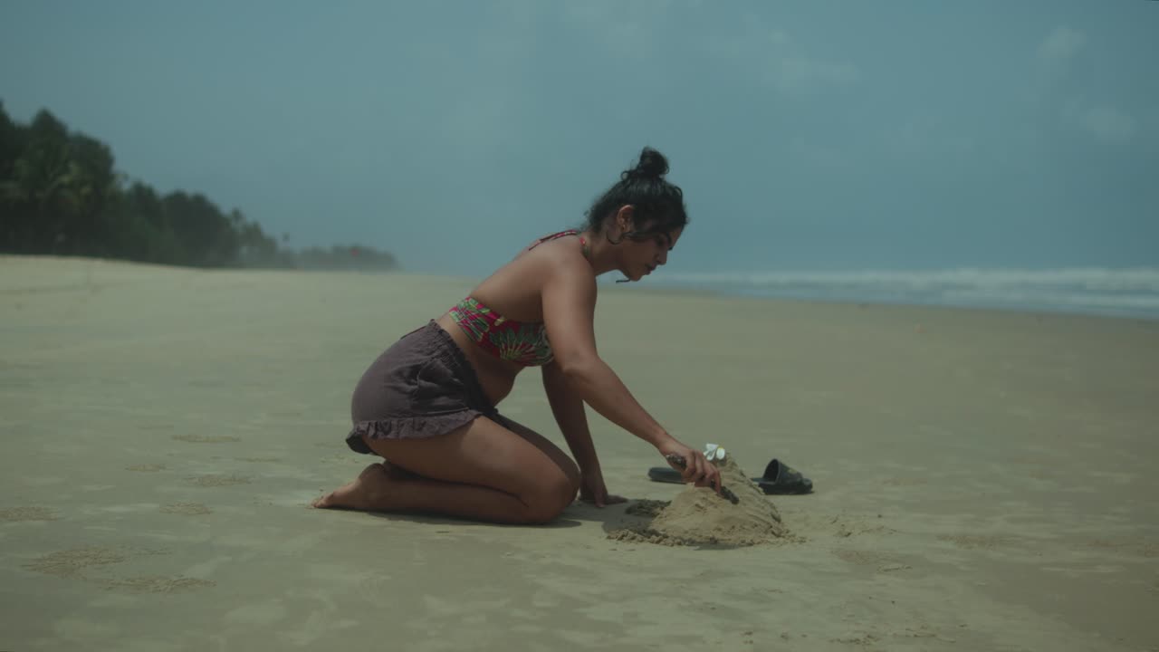 Woman building sandcastle on beach, calm solitude, creative leisure activity