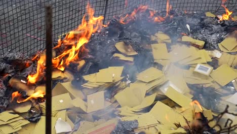 Close-up-on-fire-pit-with-paper-money-being-thrown-onto-ashes-and-flames-during-spiritual-ceremony-to-appease-ancestors-and-ghosts-filmed-in-slow-motion