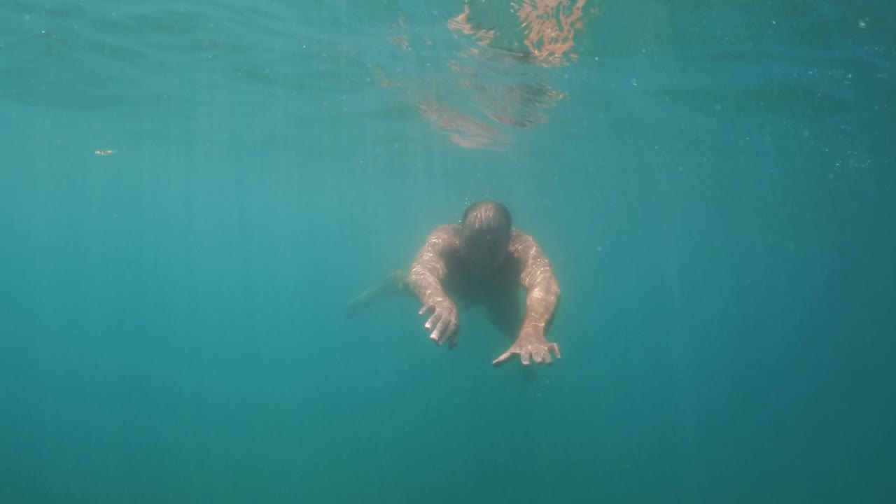 웃고 있는 동안 카메라를 향해 수영하는 무호흡증을 앓고 있는 성인 남자의 수중 슬로우 모션 장면