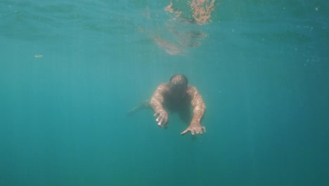 underwater slow-motion scene of adult man in apnea swimming toward camera while smiling