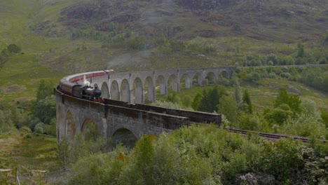 el tren de vapor de escocia se acerca en el puente del viaducto a través de las montañas.