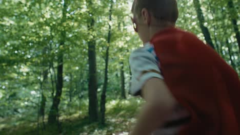 Ginger-caucasian-boy-wearing-superhero-costume-running-in-forest.