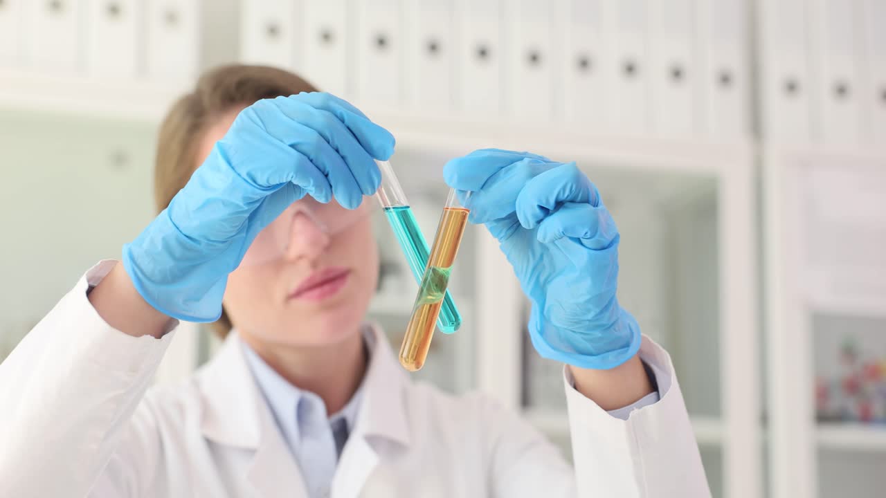 Scientist in a lab coat and safety goggles holding two test tubes