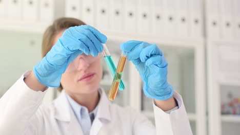 scientist in a lab coat and safety goggles holding two test tubes