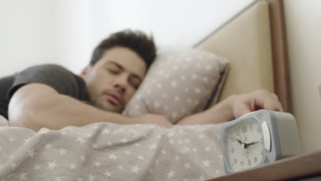 handsome man listening alarm clock through dream. man turning off alarm clock.