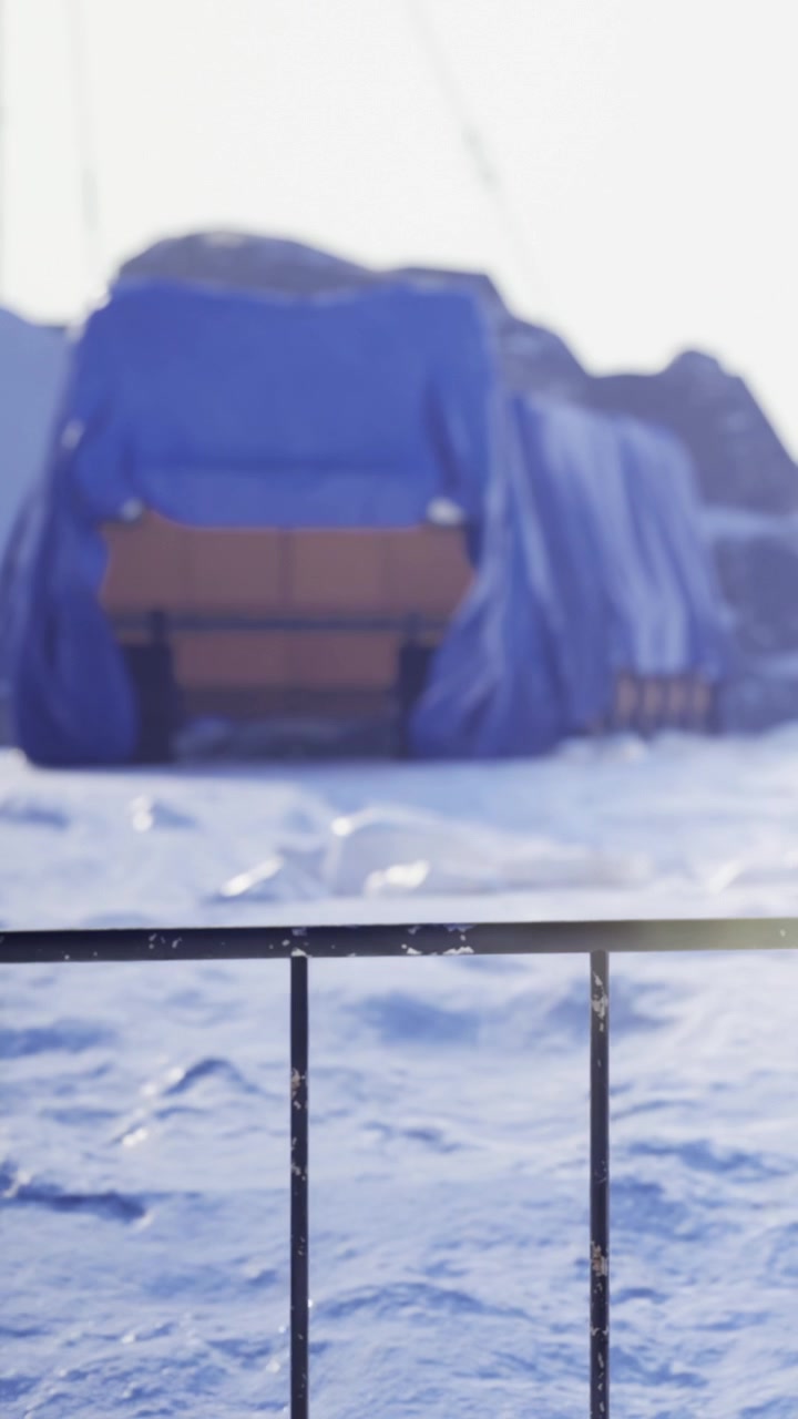 Winterlandschaft mit schneebedeckten Bänken und einer blauen Plane im Hintergrund.