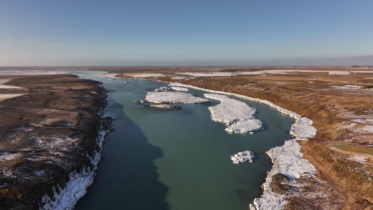 Aerial view of the Þjórsá River near Urriðafoss in Iceland, featuring floating ice and a rugged winter landscape under clear blue skies.
