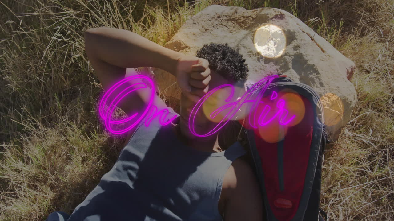 man lying on grass shielding eyes, with neon On Air overlay, lens flare in technology tutorial