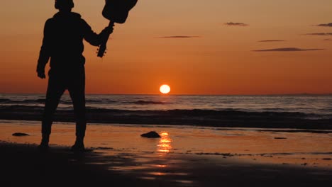 Man-running-with-guitar-in-back-sand-beach-at-sunset-22