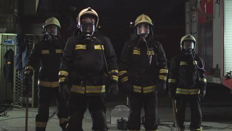 group of firefighters wearing full equipment, oxygen masks, and emergency rescue tools, circular hydraulic and gas saw, axe, and sledge hammer. smoke and fire trucks in the background.