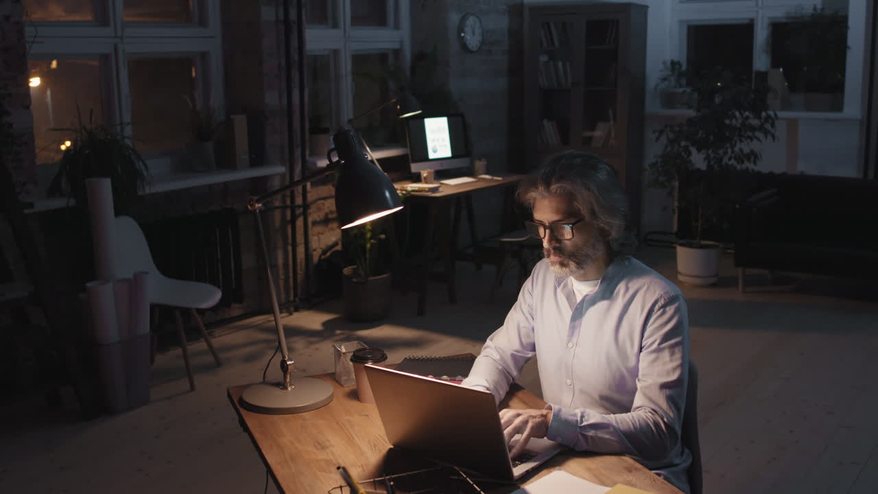 Mature man working on laptop at night in a dimly lit office