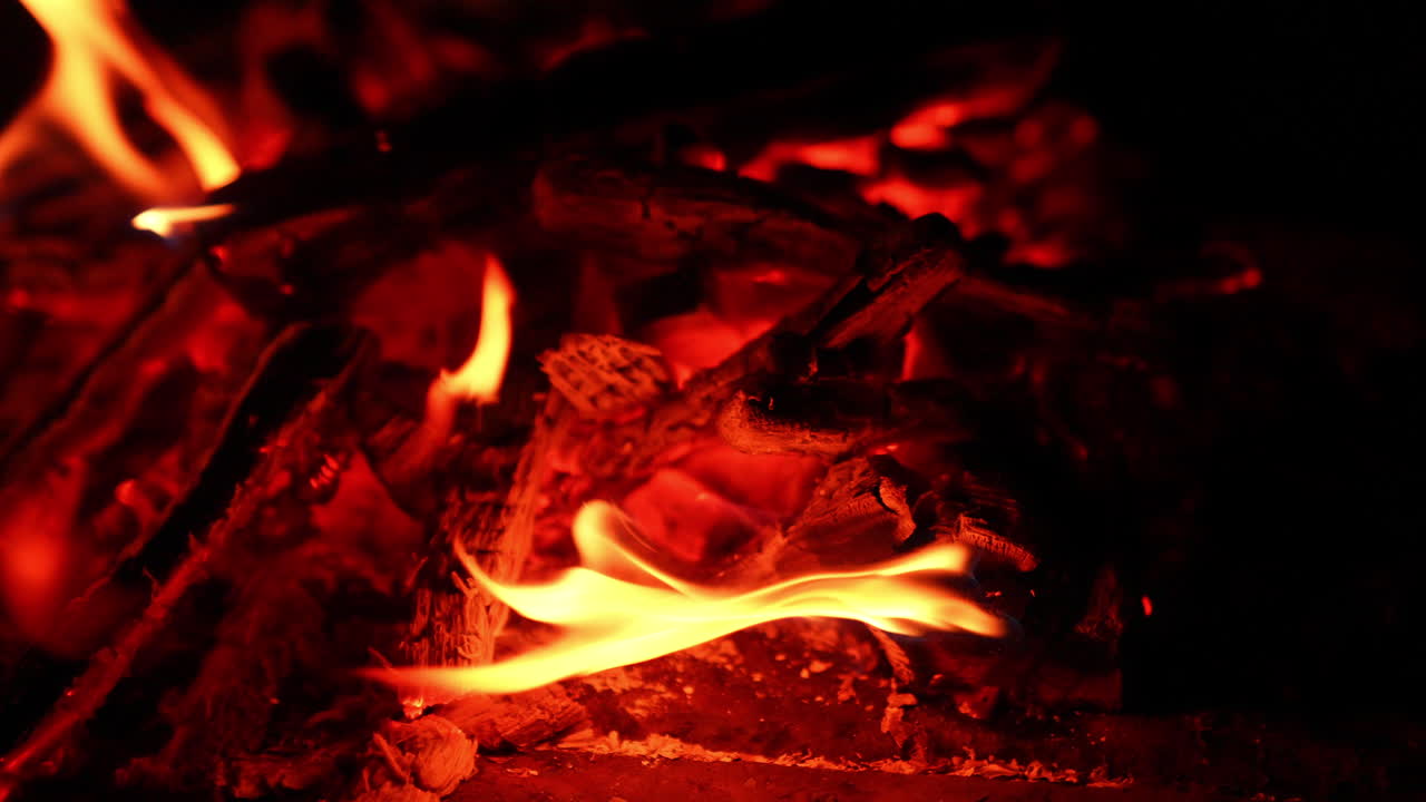 Burnt out campfire with hot red embers. Small flames appear on the charcoals. Close up.